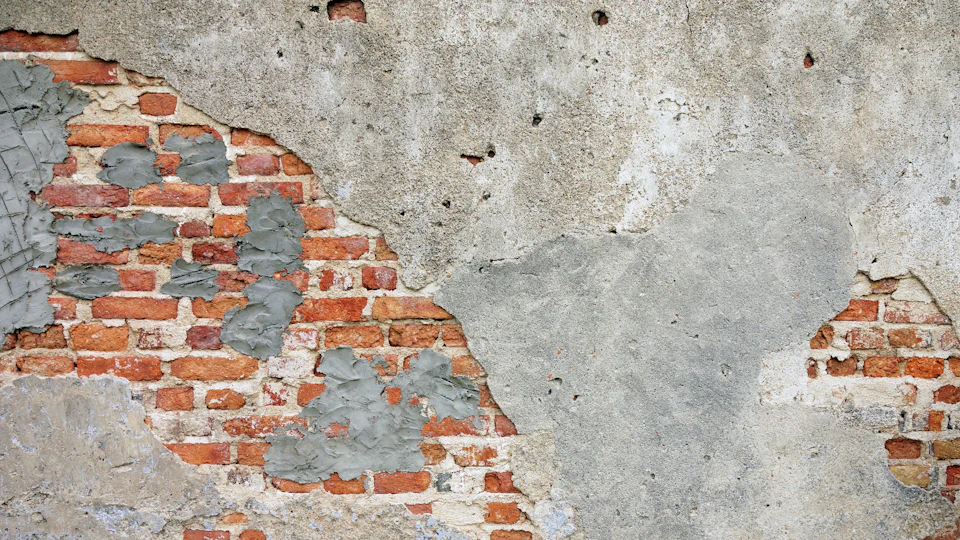 Old plaster fallen away from a brick wall in patches, the bricks showing through