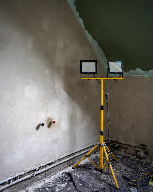 A freshly plastered wall still dark in patches, a site light on a tripod in front of it