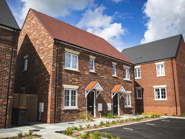 A pair of new-build brick semis with a tiled roof under a blue sky