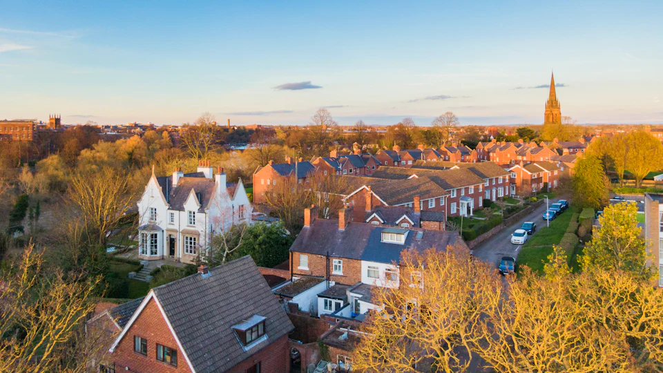 Rooftops of a market town among autumn trees at sunset, a church spire on the skyline