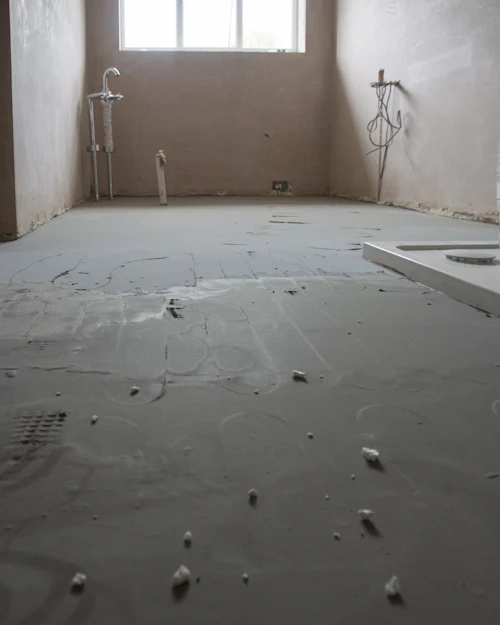 A bare room with newly plastered walls drying to a pale pink, the floor covered