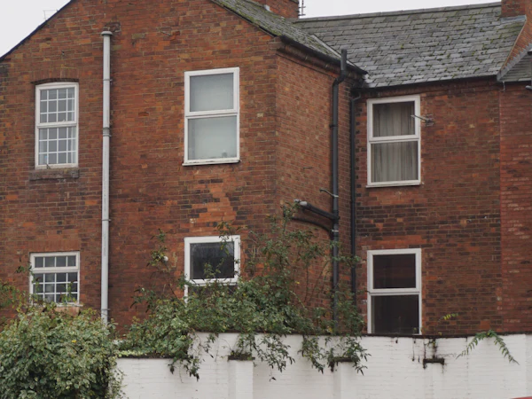 The side of a red brick house with two chimneys and white sash windows
