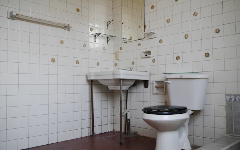 Before: a tired bathroom in old white tiles with a pattern of small motifs, a pedestal basin and a WC