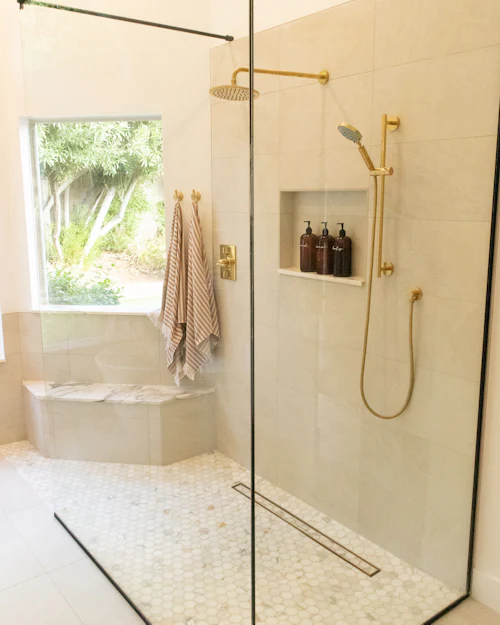 A bright shower with a pebble mosaic floor, a tiled bench and brushed brass fittings