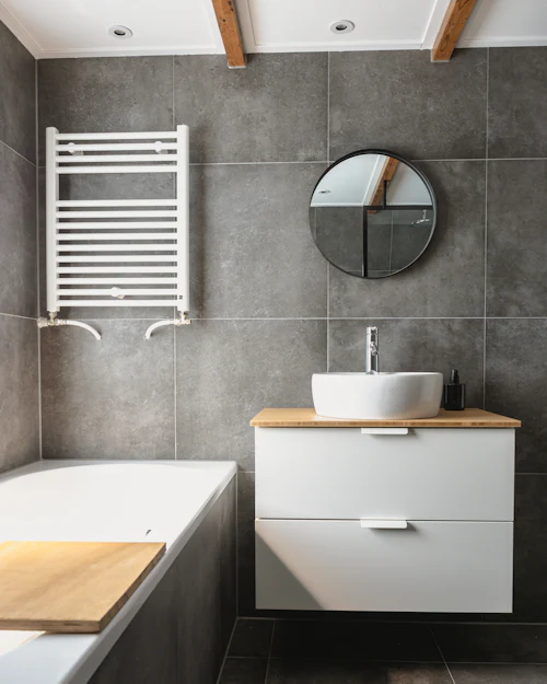 A grey porcelain bathroom with a white vanity on an oak top, a bath and a towel radiator