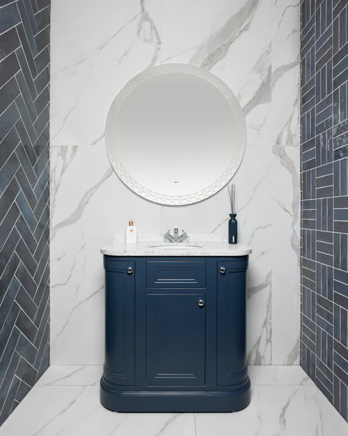A navy vanity between two strips of dark blue herringbone tiles, marble-look porcelain behind