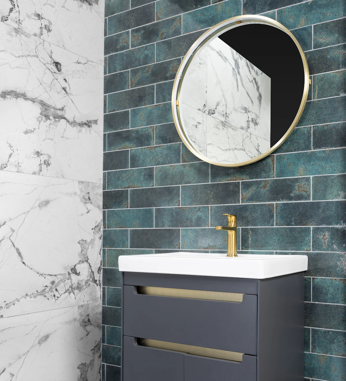 A finished bathroom: green brick-bond tiles behind a round brass mirror, a white basin and a grey vanity, marble-look porcelain on the side wall