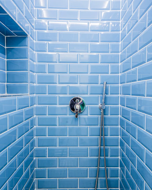 A shower lined in glossy blue metro tiles laid in brick bond, a chrome valve on the wall