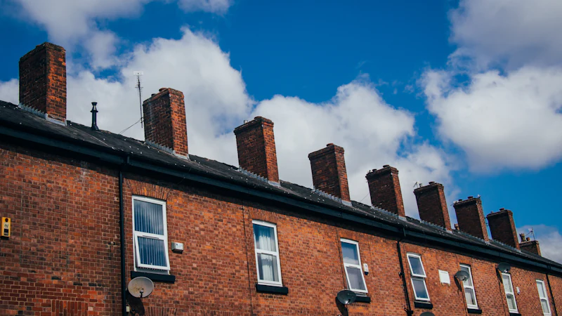 A row of red-brick Victorian terraced houses with their chimneys against a blue sky