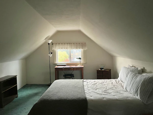 A loft bedroom with a double bed under a sloped ceiling and a desk under the window