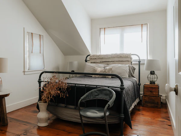 A white loft bedroom with an iron bed under the slope and a window at the far end