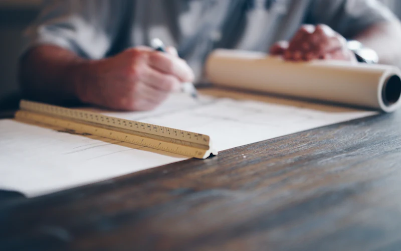 Hands drawing on a sheet of plans with a scale rule