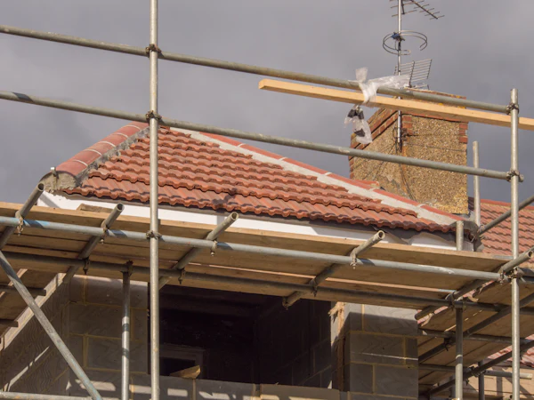 Scaffold along the eaves of a tiled roof, a chimney stack beyond