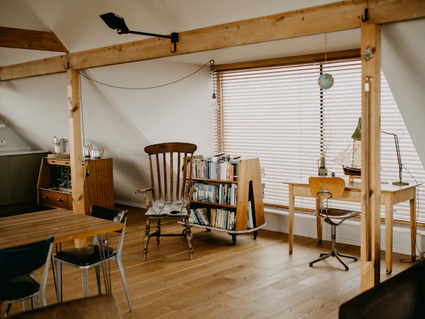 A loft study with exposed timber posts, a desk under the window and shelves of books