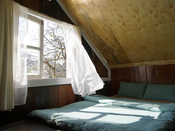 Morning light through an open window across a low bed in a timber-lined loft